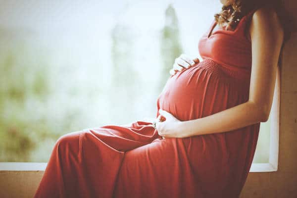 Schwangere Frau in rotem Kleid sitzt am Fenster.